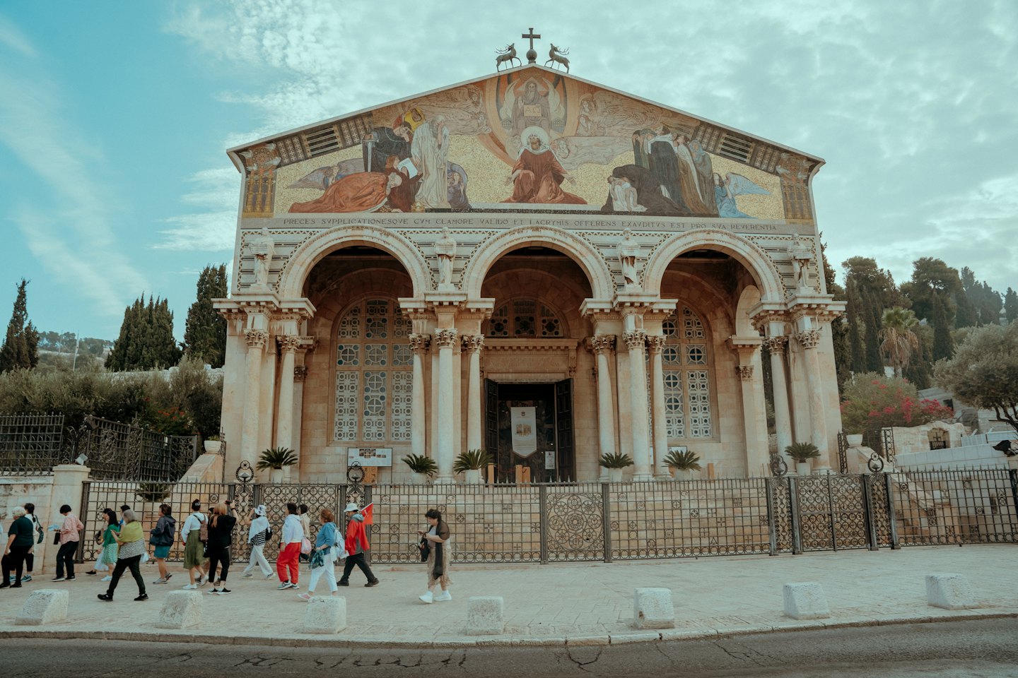 People walking past a grand church with a mosaic facade.